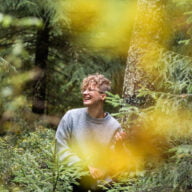 Nainen hymyilee metsän ympäröimänä.