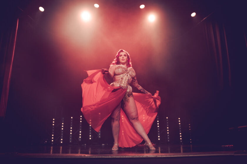 Kuvassa burleskiesiintyjä Olivia Rouge seisoo lavalla parrasvalojen alla levittämässä punaisen hameen kankaita