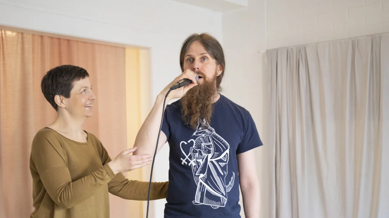 Katja Harilo ohjaa mikrofoniin laulavaa miestä.