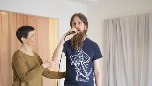 Katja Harilo ohjaa mikrofoniin laulavaa miestä.