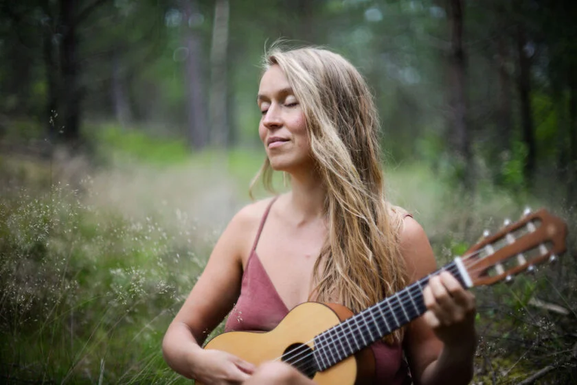 Nainen soittaa kitaraa kesäisessä metsässä