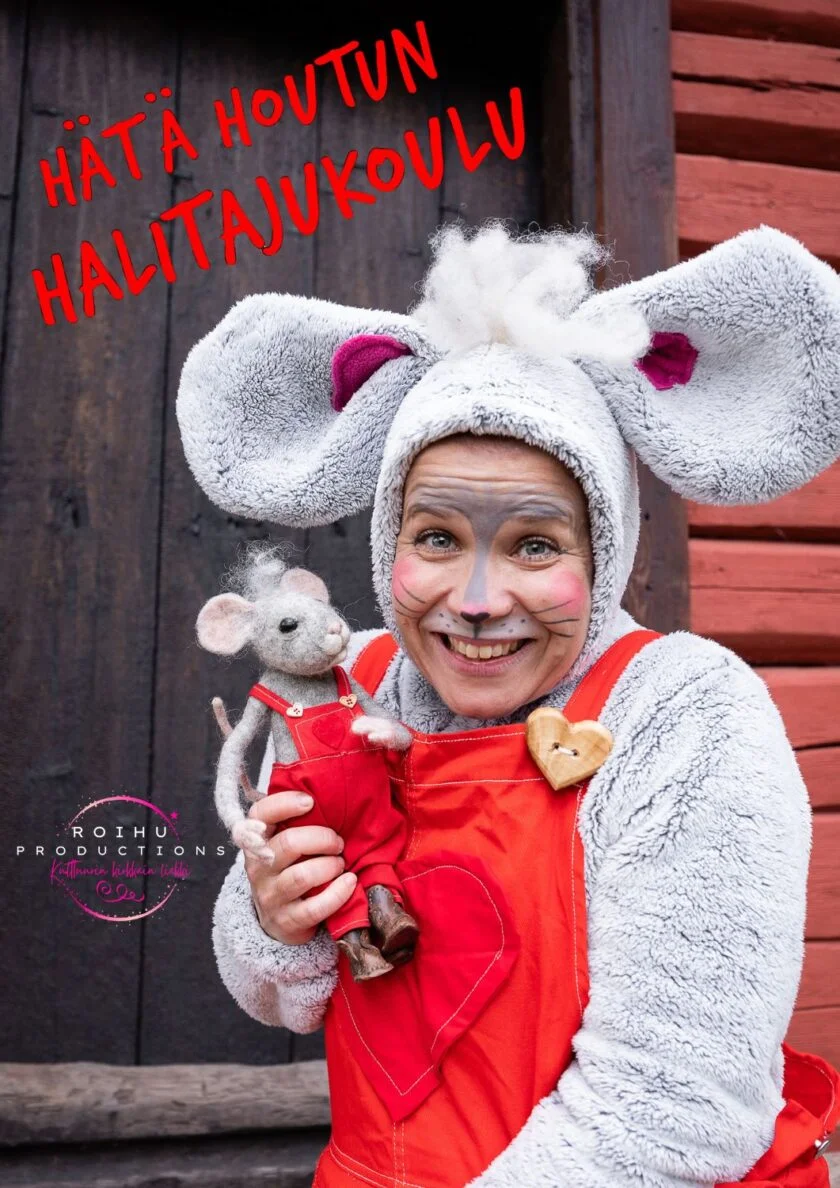 Harmaaseen hiiripukuun pukeutunut nainen hymyilee ja katsoo kameraan. Kädessään hänellä on itseään muistuttava hiirinukke punaisessa haalarissa.