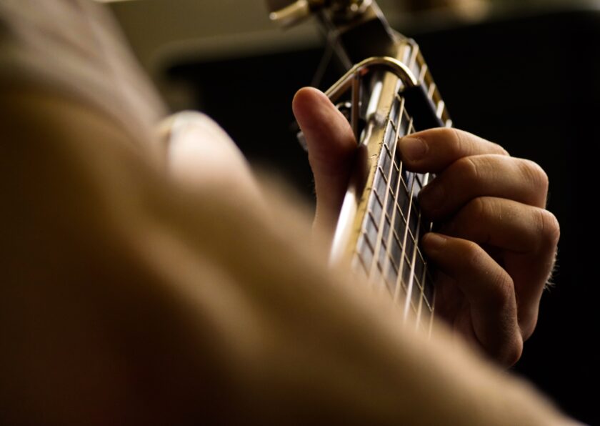 Kuvassa kitaran kaula, jonka ympärillä on ihmisen sormet.