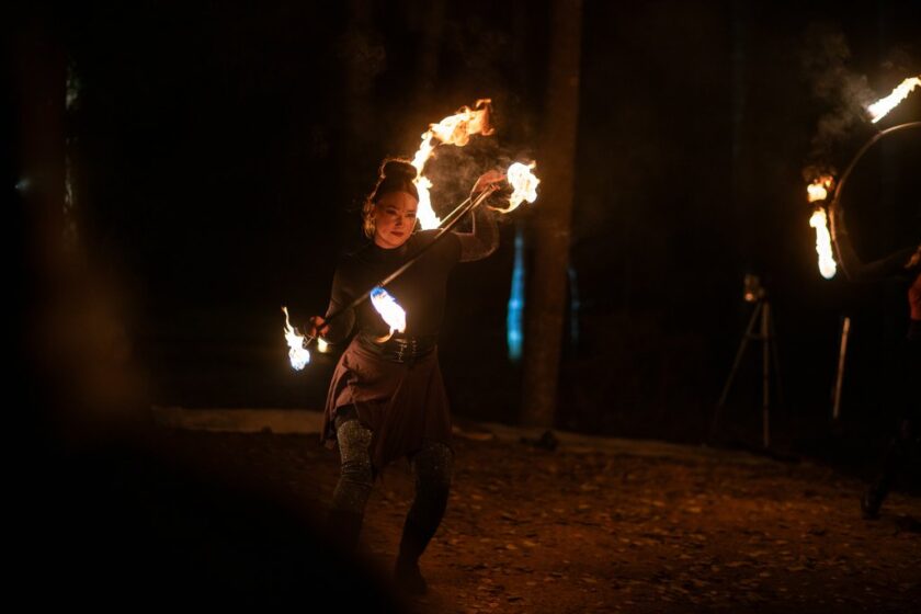 Piemä metsä, esiintyjällä vanne vinottaina käsissä. Liekit luovat kuvion.