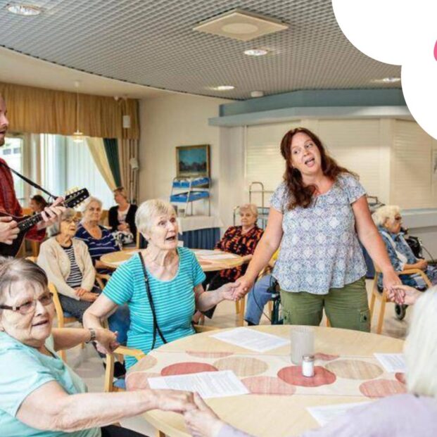 Kuvassa muusikot soittavat ja laulavat ikäihmisten palvelukodin salissa yhdessä asukkaiden kanssa. Keskellä on pyöreä pöytä, jonka ympärillä istuvat henkilöt pitävät toisiaan käsistä kiinni muodostaen laulavan piirin. Vasemmassa reunassa on kitaransoittaja ja taaempana lisää laulavia asukkaita. Kuva on värikäs ja oikeassa yläreunassa on valkoisen pilven päällä Uulun vaaleanpunainen logo.