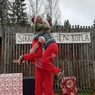 Kuvassa kaksi tontuiksi pukeutunutta on kolmannen, myös tontuksi pukeutuneen hartioilla.