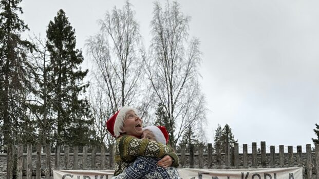 Kuvassa kaksi tontuiksi pukeutunutta on kolmannen, myös tontuksi pukeutuneen hartioilla.