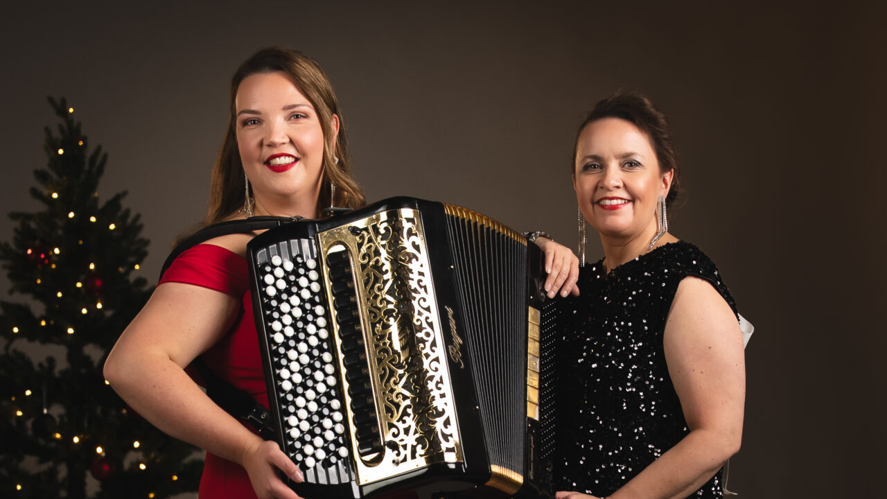 Henna Leppänen on kuvan vasemmassa reunassa harmonikka sylissä ja laulaja Johanna Debreczeni kuvan oikealla puolella. Kuvan tunnelma on jouluinen ja taustalla on joulukuusi.