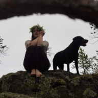 Kuvassa laulaja-lauluntekijä Anni istuu kalliolla vieressää musta koira.